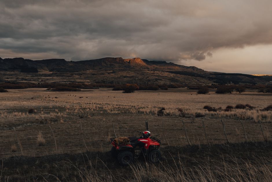 A scenic view of farmland with an ATV and mountains under a dramatic sunset sky.