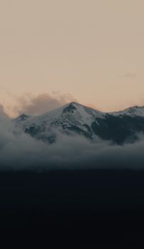 Snow-capped mountains shrouded in mist during sunrise, creating a serene landscape.