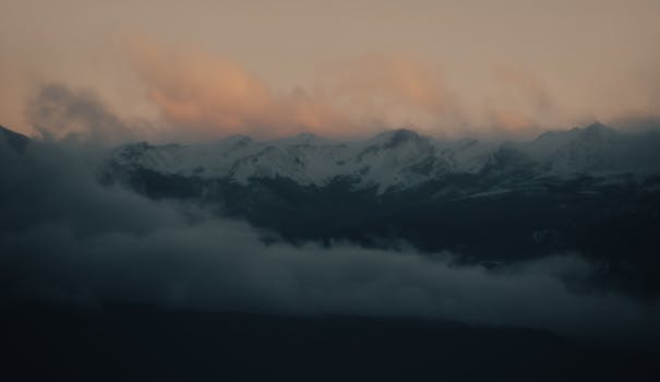 Breathtaking view of snow-capped mountains enveloped in mist under a twilight sky.