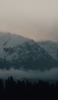 A tranquil view of snow-covered mountains with mist and fog at dusk.