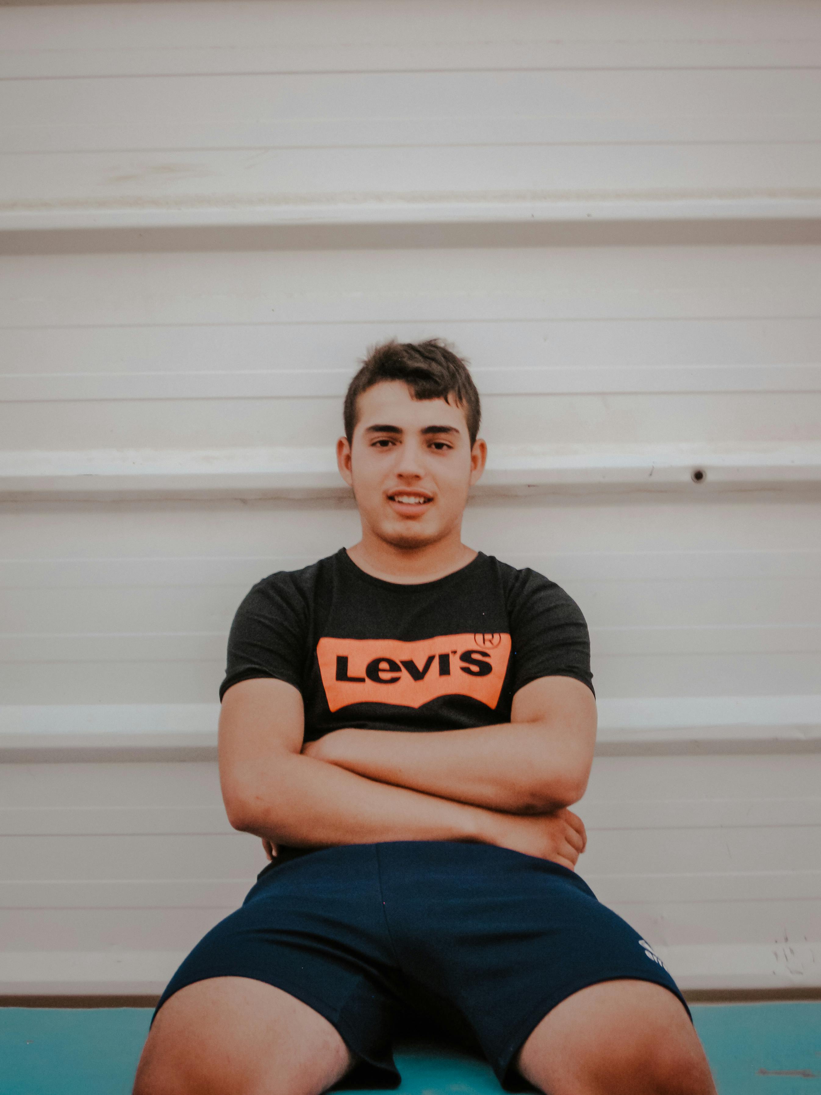 Confident young man in casual wear sitting with crossed arms indoors.