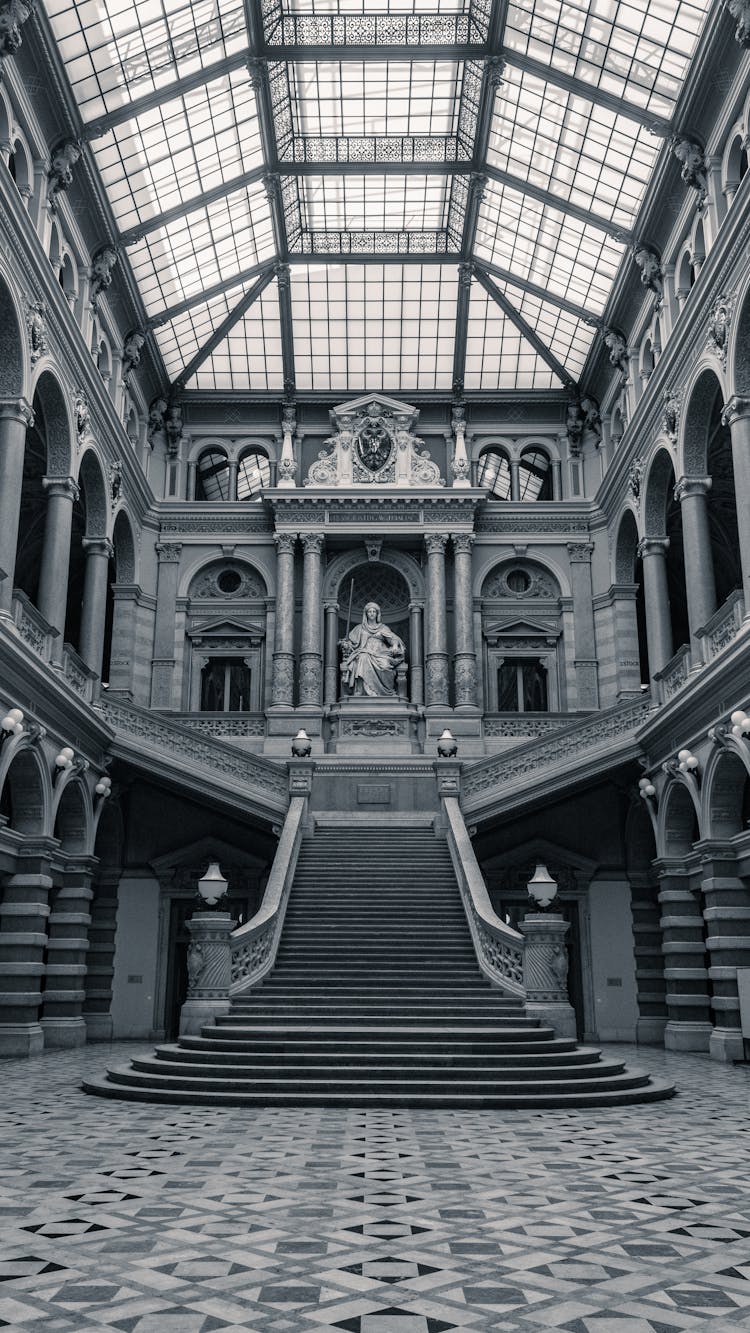 Grayscale Photo Of A Woman Statue Sitting Near Staircase