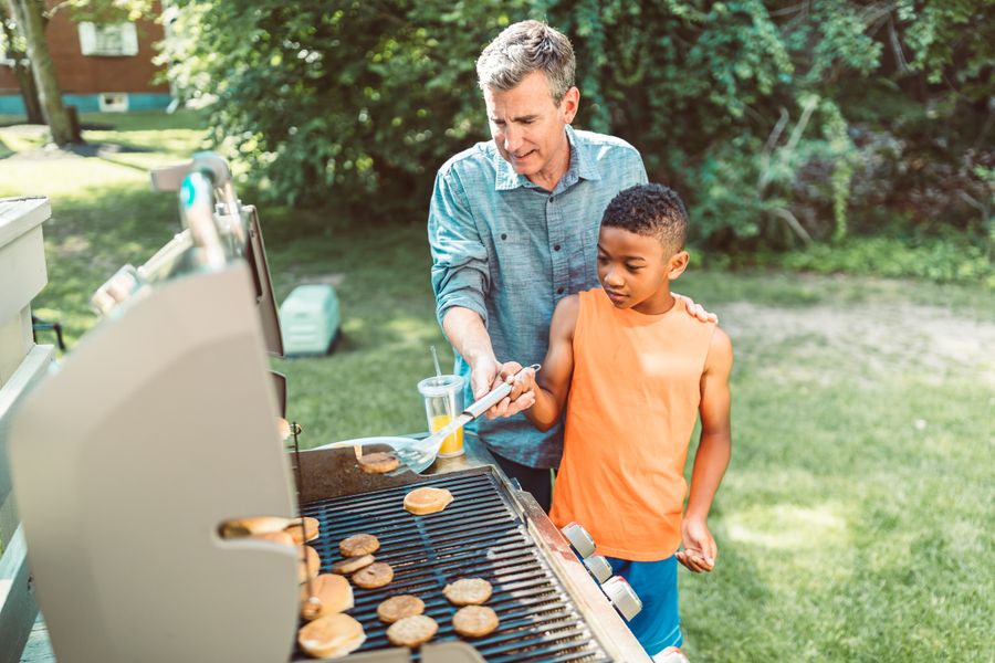 A father and son grilling burgers together on a propane barbecue outdoors