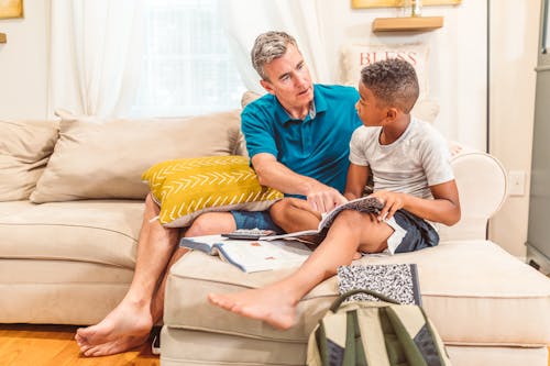 Free Dad and Son Sitting on a Couch While Reading a Book Stock Photo