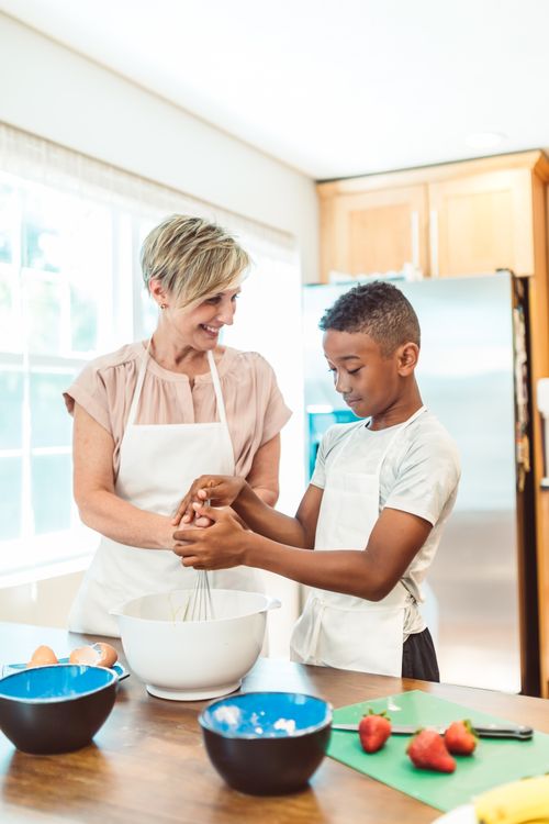 Free Smiling mother and son baking together in a sunlit kitchen, fostering family bonding and learning. Stock Photo