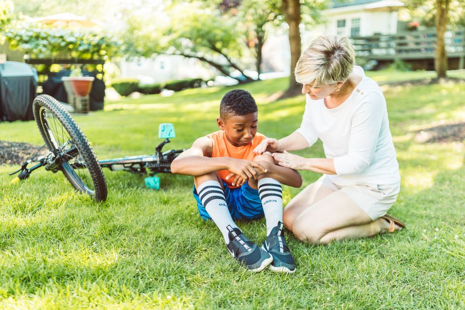 A mother cares for her son with a minor wound after a bike fall on a sunny day.