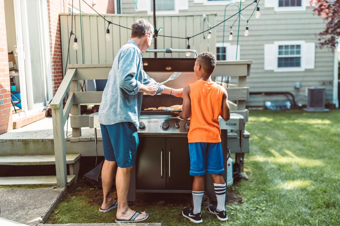 A father and son grill together on a sunny backyard barbecue