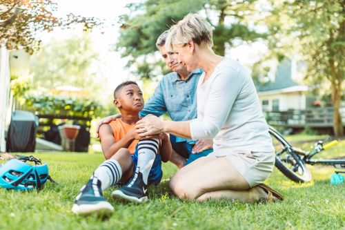 Free Parents comforting their injured son after a biking accident in a sunny backyard. Stock Photo