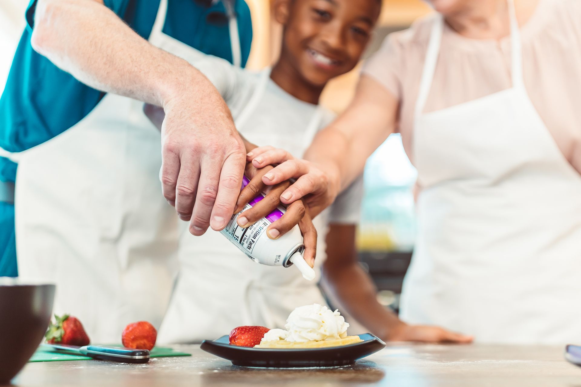 A family enjoying quality time while preparing a strawberry and whipped cream dessert together.