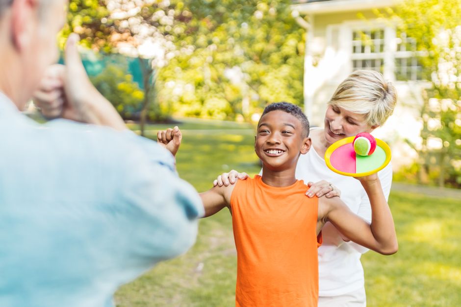Family playing catch outdoors in sunny backyard with child in orange shirt