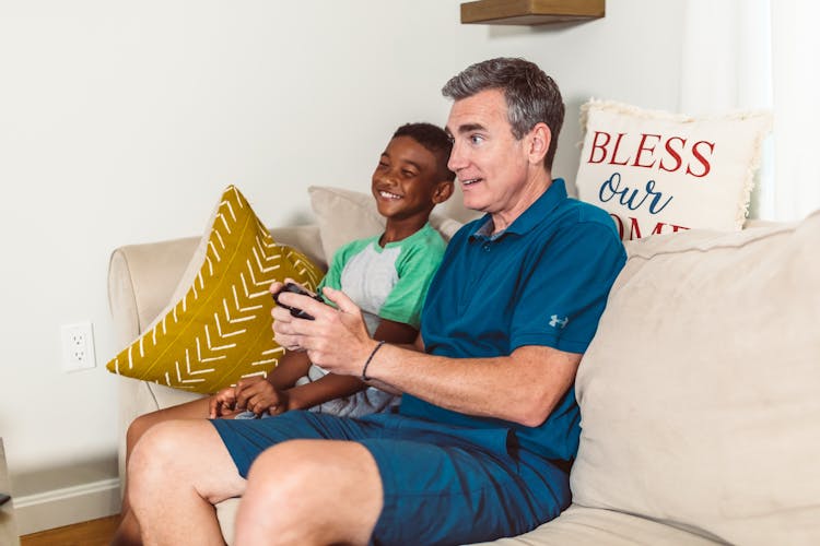 Father And Son Sitting On A Couch While Holding Game Controller