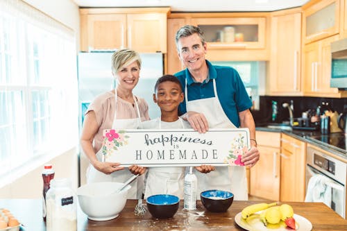 A Happy Family Wearing Apron Standing in the Kitchen while Holding a Signage