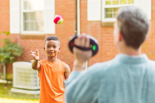 A Boy in Orange Tank Top Shirt Tossing a Ball to a Person Holding a Paddle Catch