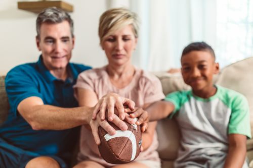 Free A diverse family bonding while holding a football together on a couch indoors. Stock Photo