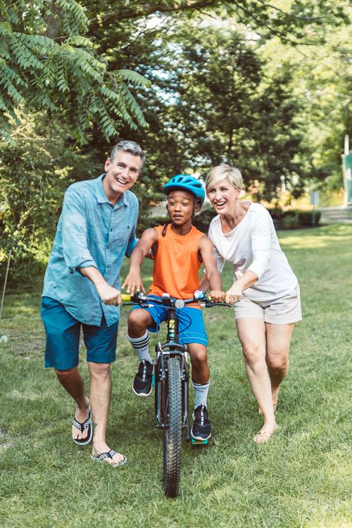 Free Smiling couple teaching a boy to ride a bicycle in a sunny park setting. Stock Photo