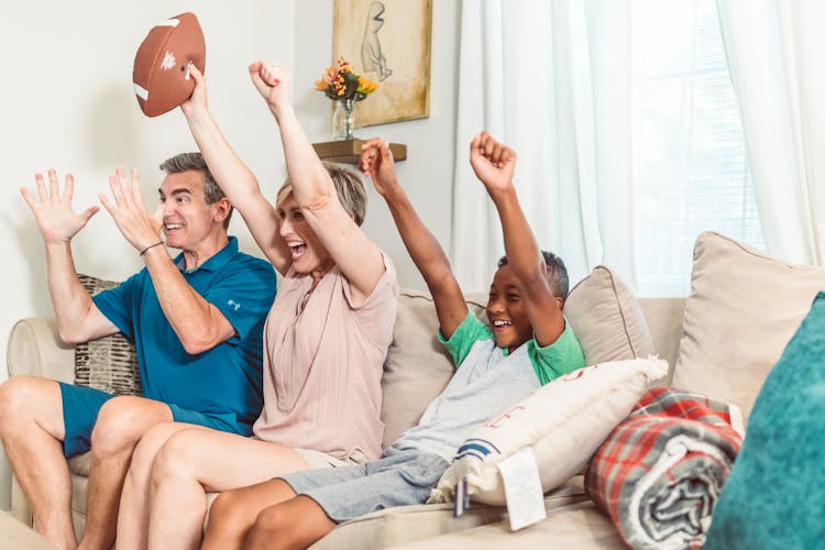 A Happy Family Sitting On A Couch While Cheering Together