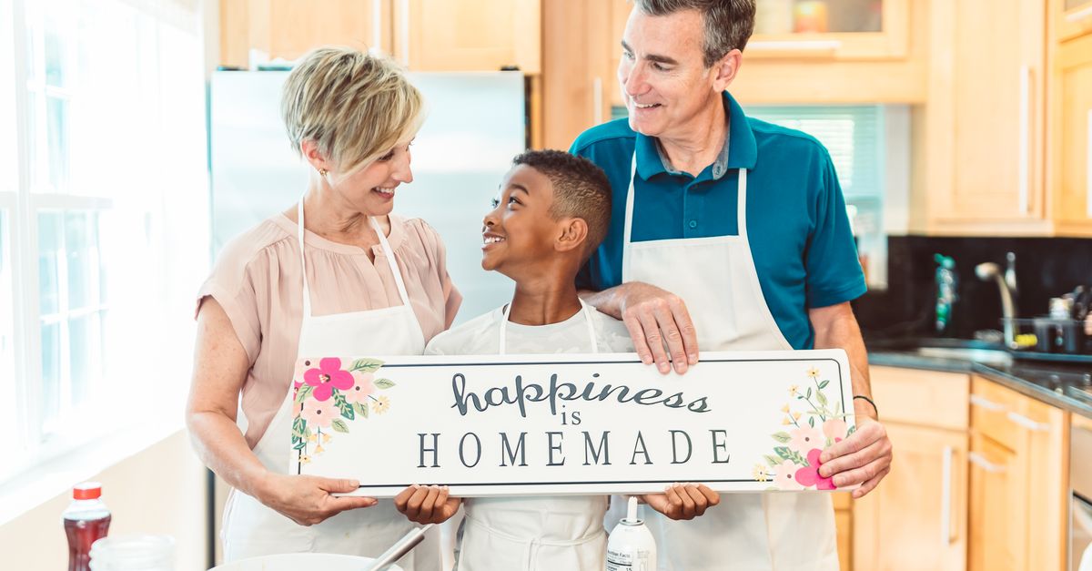 A family of three bonding in the kitchen, holding a 'happiness is homemade' sign.