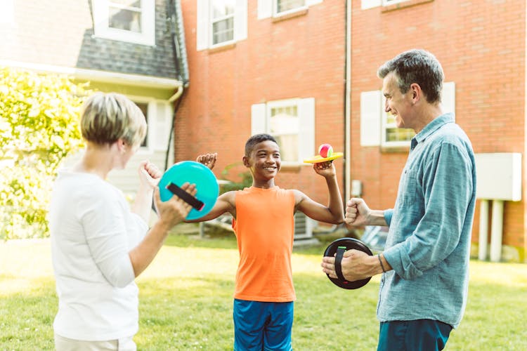 A Happy Family Standing On The Backyard While Holding Flying Discs