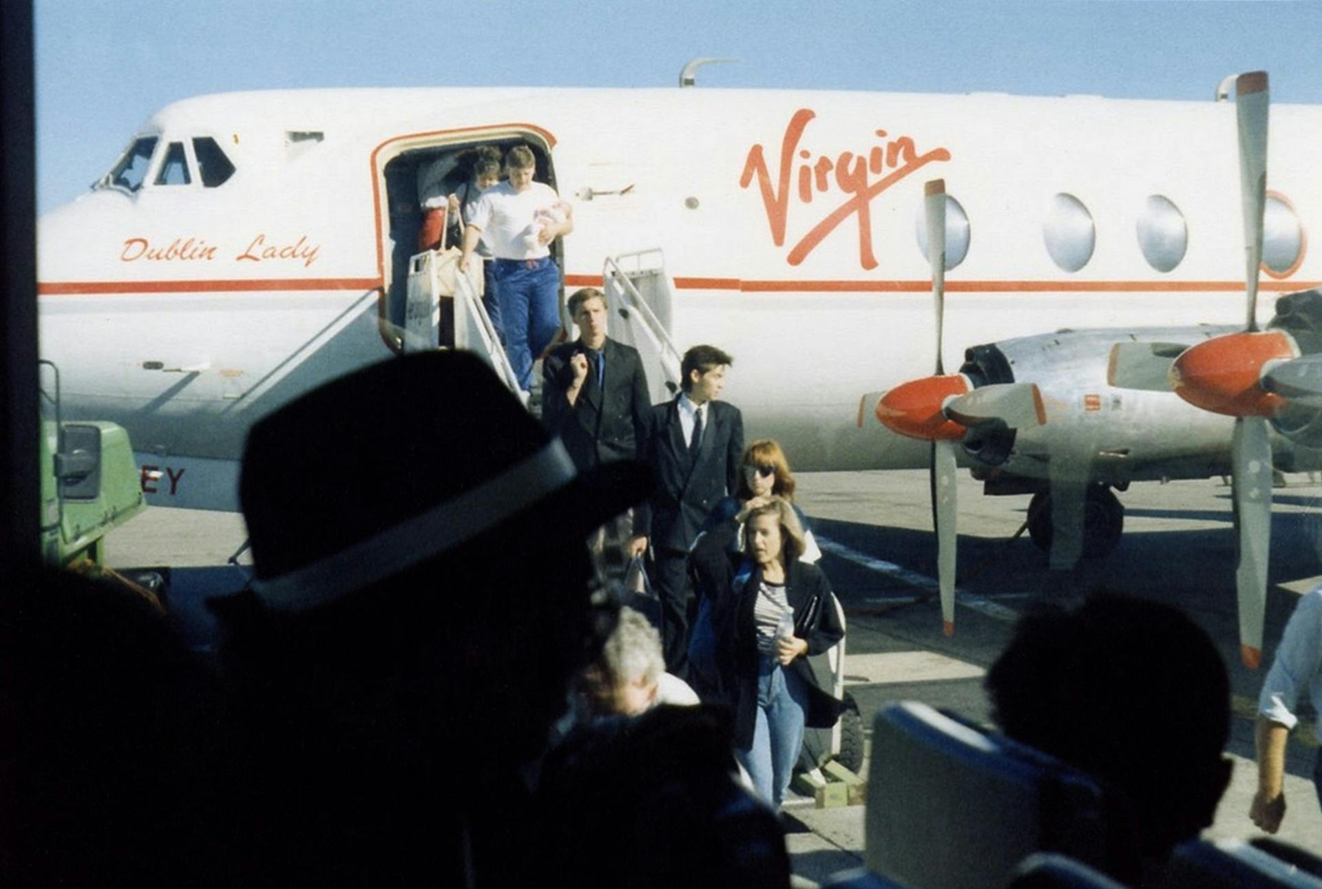 Passengers exiting a Virgin aircraft titled 'Dublin Lady' at Dublin Airport on a clear day.