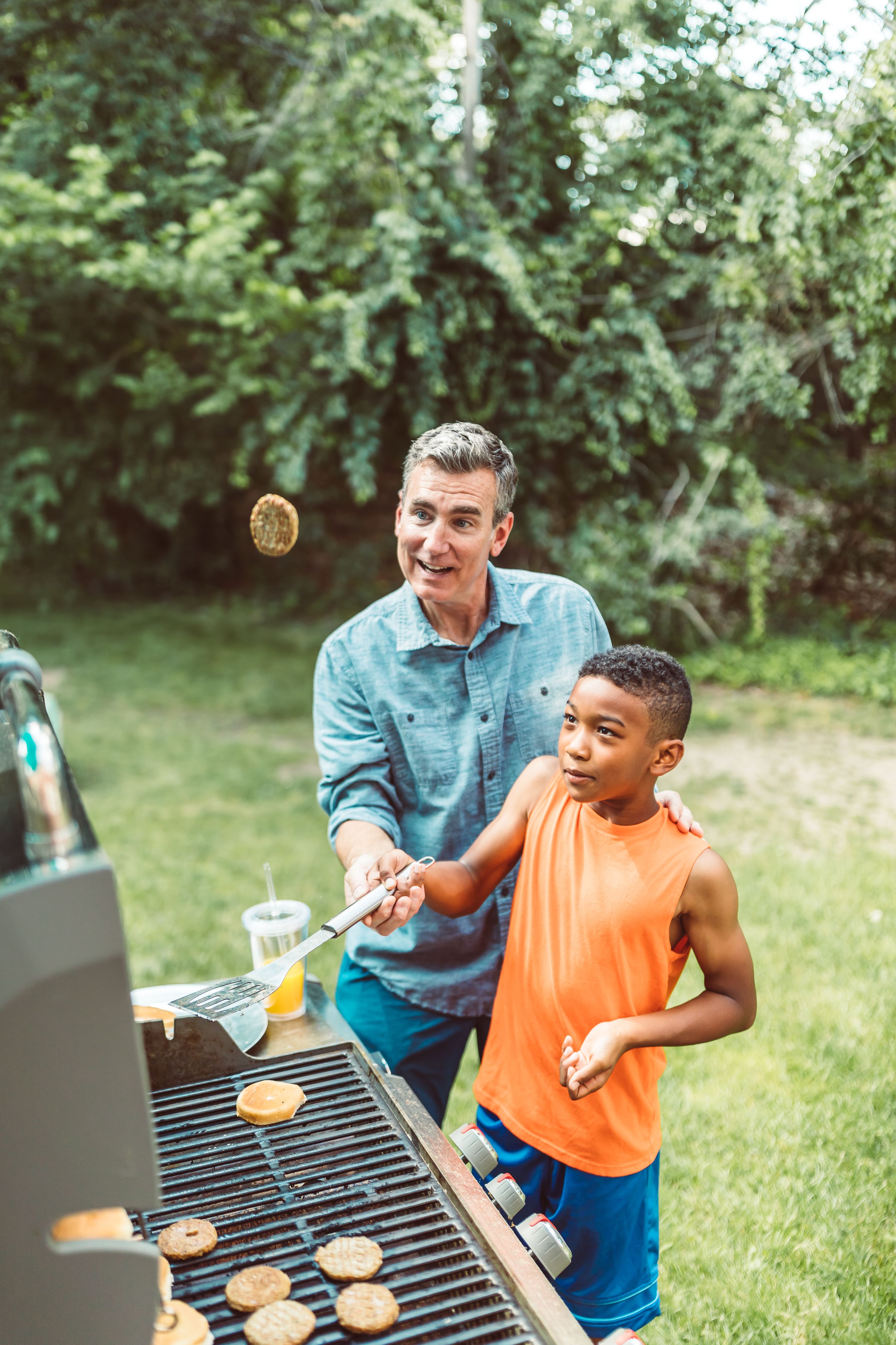 Father teaching son how to grill burgers during a fun backyard barbecue.
