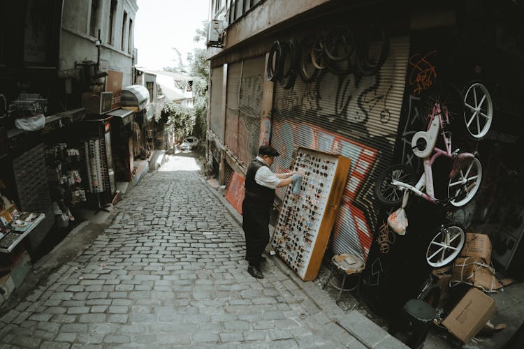 Man Standing On Cobblestone Street Near A Wooden Display Stand