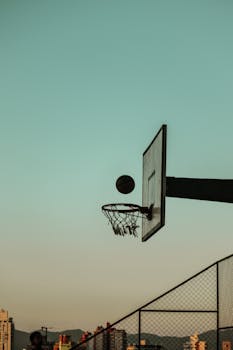 Low angle shot of a basketball in silhouette against a clear sky at dusk, emphasizing outdoor sports.