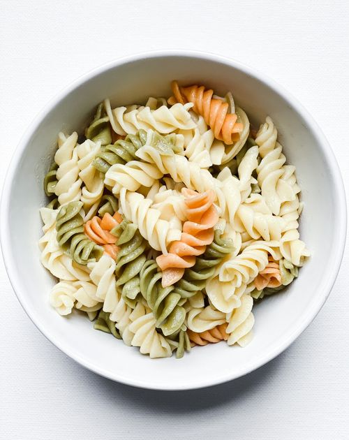 Free Close-up of colorful rotini pasta mix in a white bowl, featuring orange, green, and white spirals. Stock Photo
