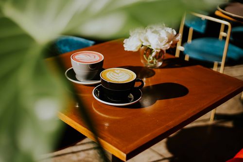 Free Two coffee cups with beautiful latte art sit on a wooden table with floral decor. Stock Photo
