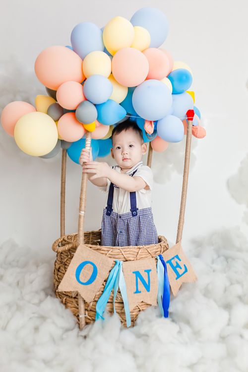Free A cute child in a hot air balloon themed setup with colorful balloons and a basket. Stock Photo