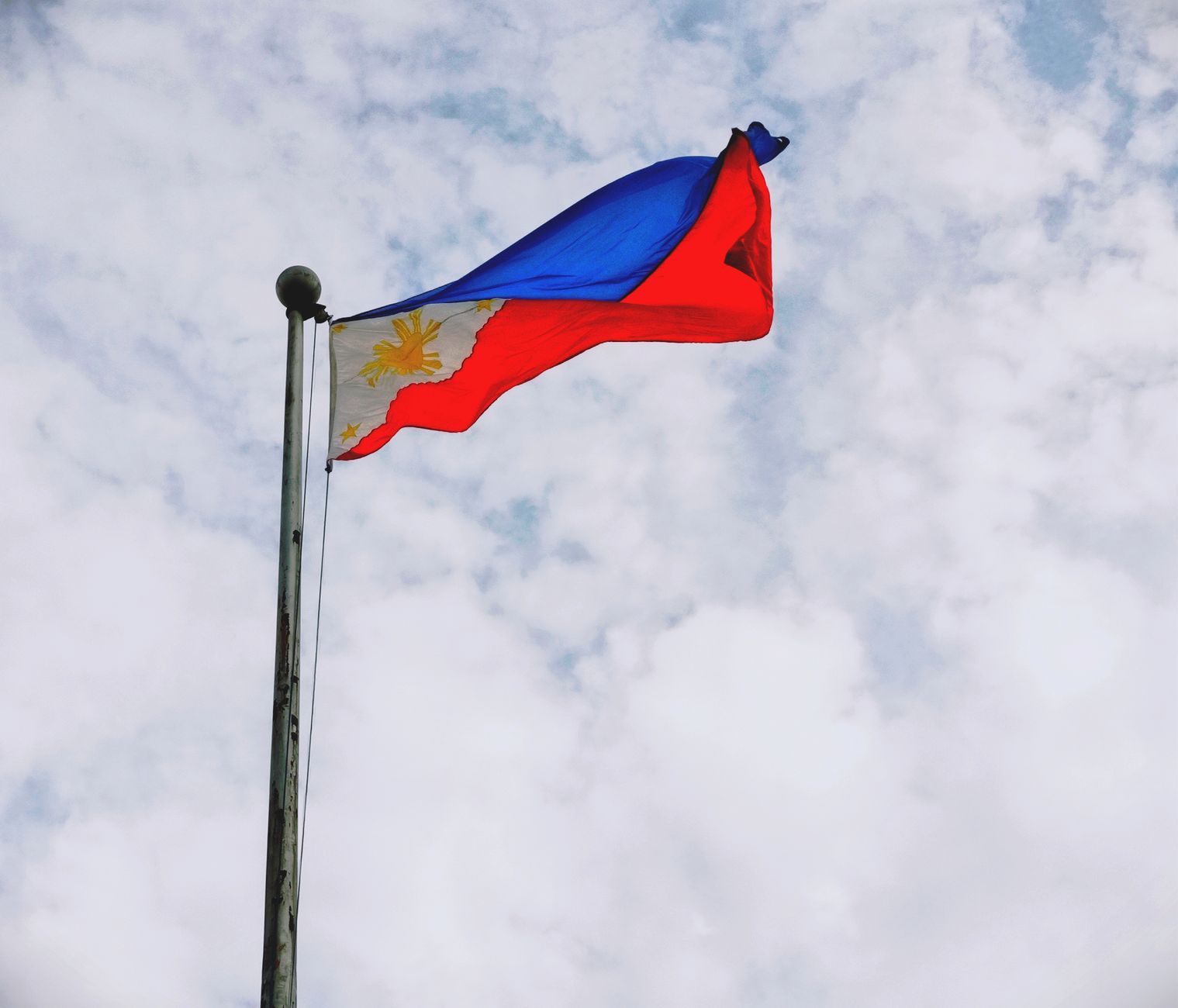 Dynamic view of the Philippine flag waving on a flagpole against a cloudy sky in Sorsogon City, Philippines.