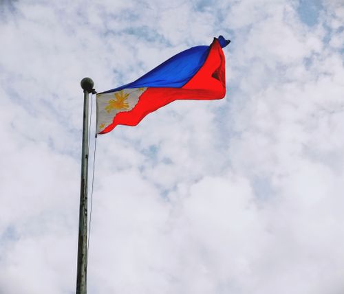 Free Dynamic view of the Philippine flag waving on a flagpole against a cloudy sky in Sorsogon City, Philippines. Stock Photo