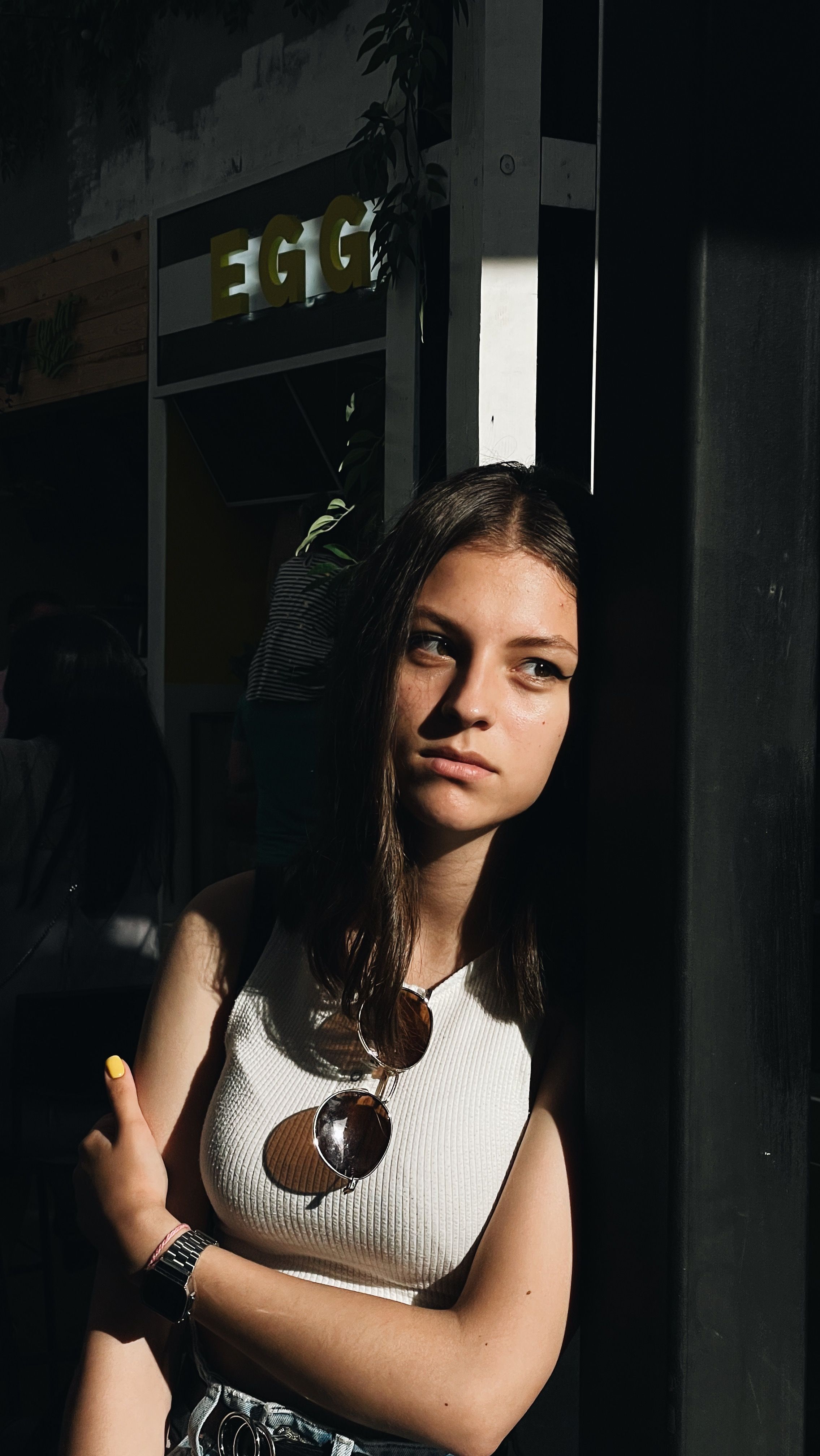 A young woman is posing thoughtfully in an urban environment with strong shadows, creating a dramatic mood.