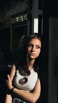 A young woman is posing thoughtfully in an urban environment with strong shadows, creating a dramatic mood.