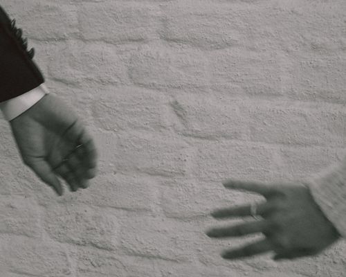 Free Monochrome image capturing the symbolic gesture of reaching hands against a brick wall. Stock Photo