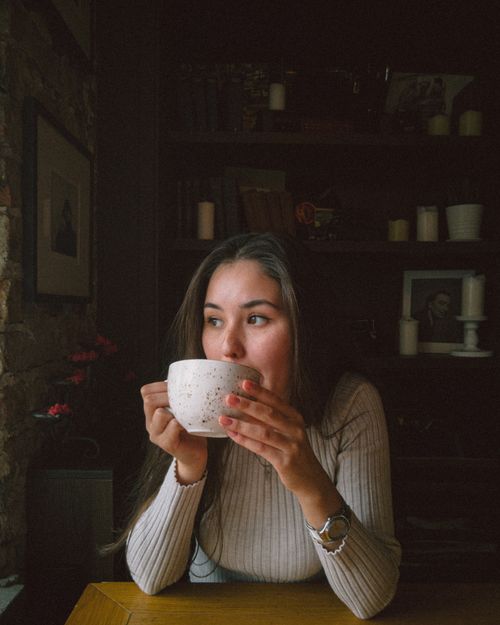 Free Young woman in a knitted sweater sips coffee indoors with warm lighting and rustic decor. Stock Photo
