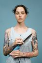 A Tattooed Woman Holding a Knife while Looking Down