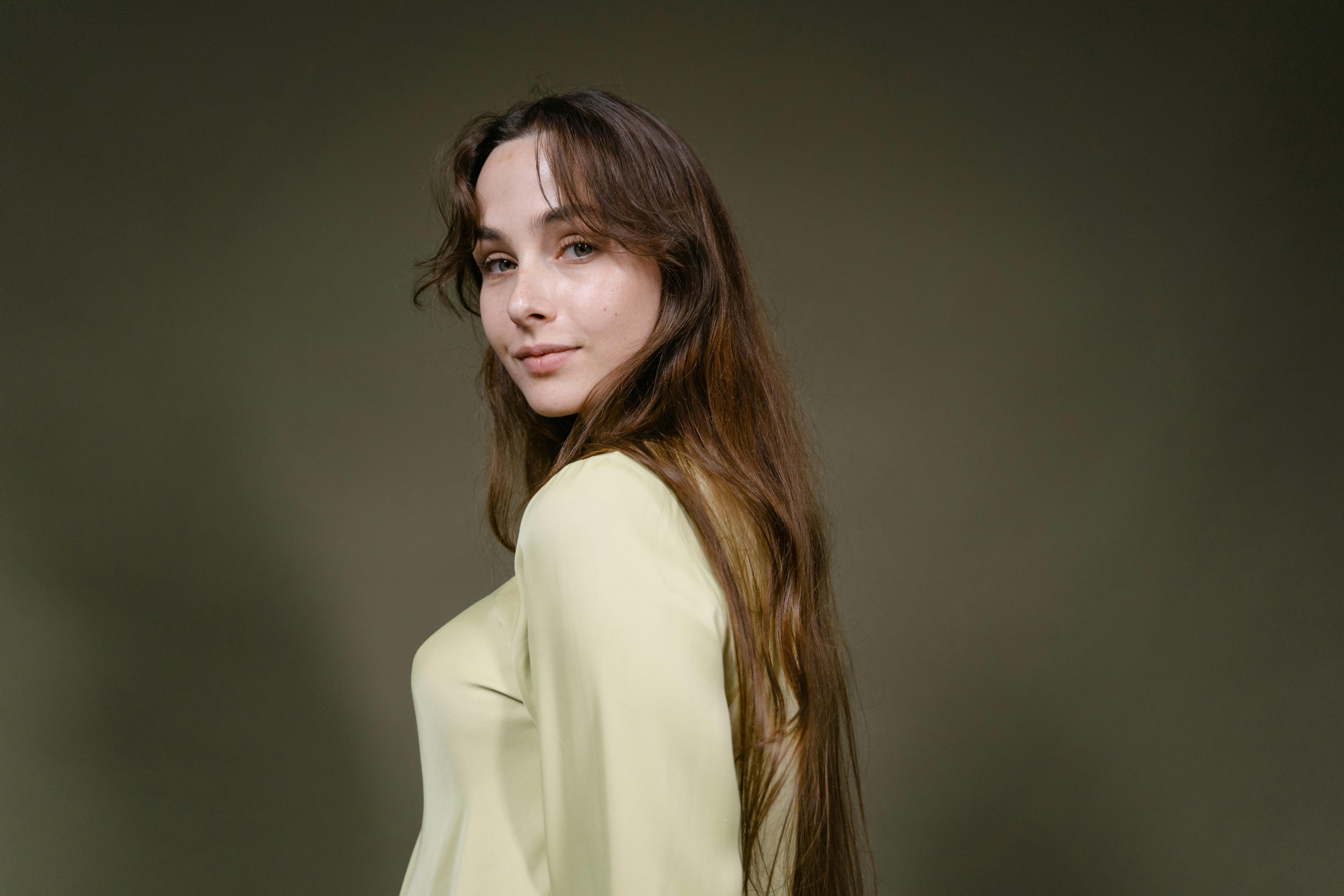 Elegant woman with long brown hair in a yellow blouse, posing in studio setting.