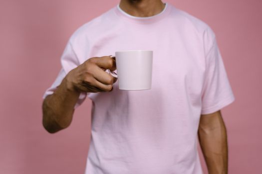 Close-up of a man holding a ceramic mug with a pink background. Casual and minimalist style.