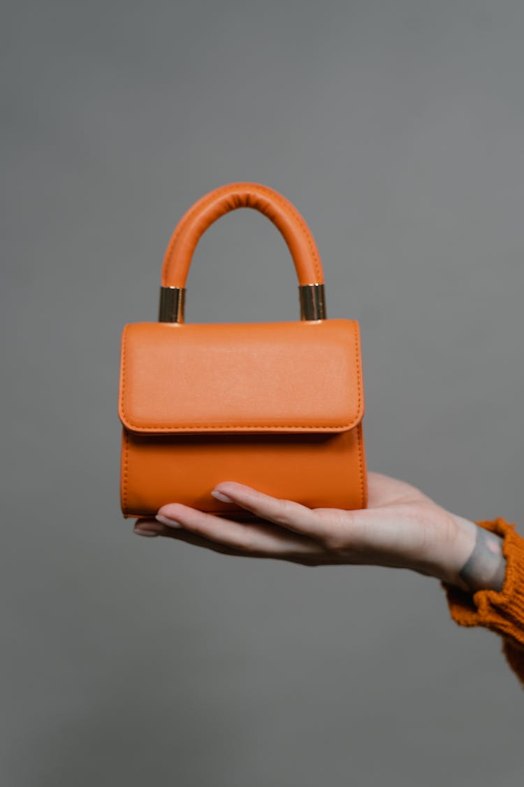 Person Holding A Mini Orange Leather Handbag