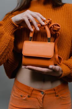 Model showcasing a vibrant orange knitted sweater and matching handbag, perfect for fashion insights.