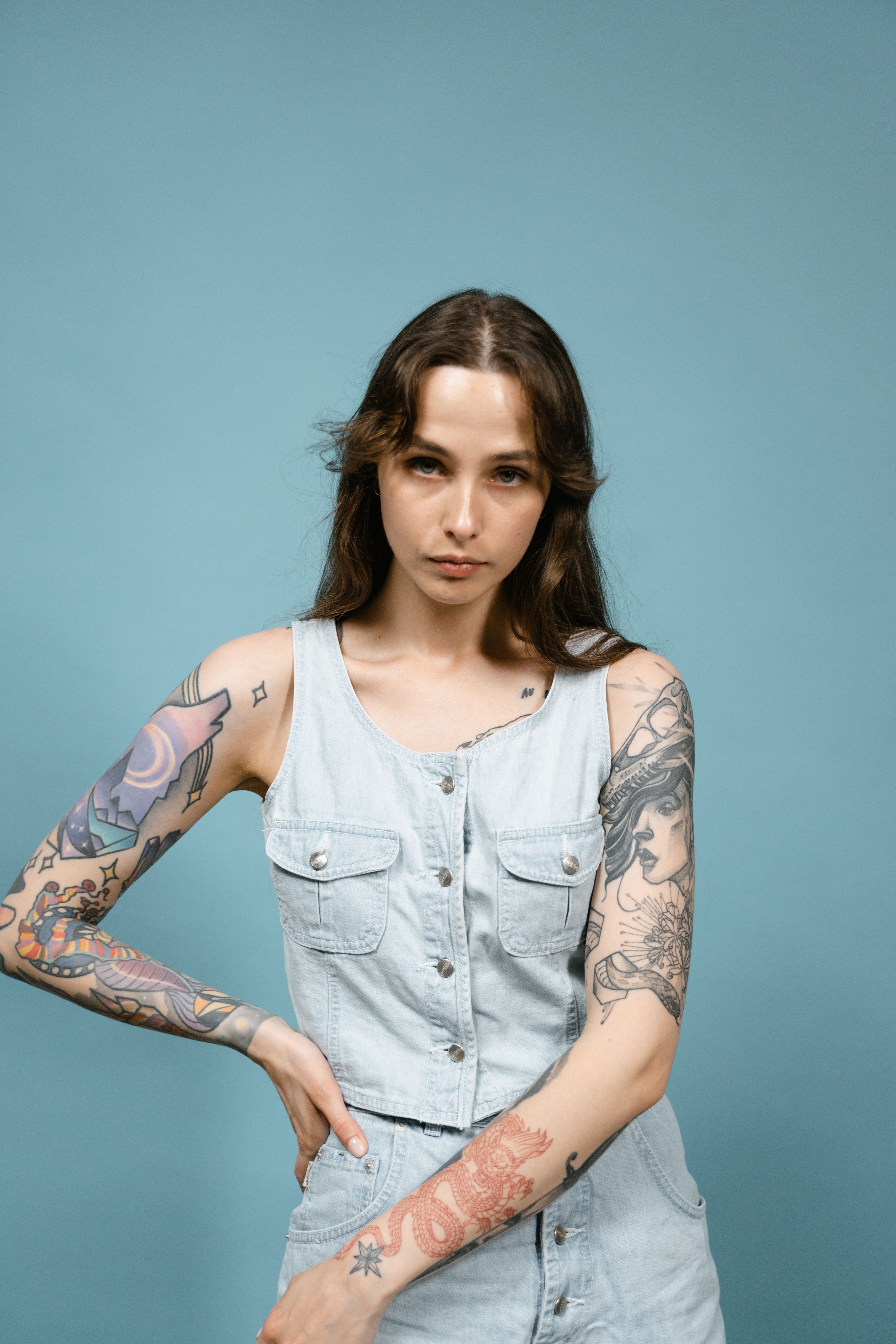 Portrait of a tattooed woman in denim against a blue backdrop in a studio setting.