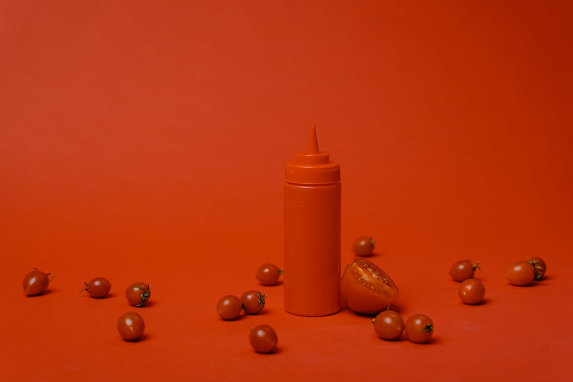 Condiment Plastic Bottle Surrounded with Cherry Tomatoes on a Red Surface