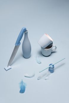 A creative composition of kitchen items and feathers on a pastel blue background.