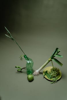 Artistic arrangement of green vegetables, fruits, and a bottle in a still life photo.