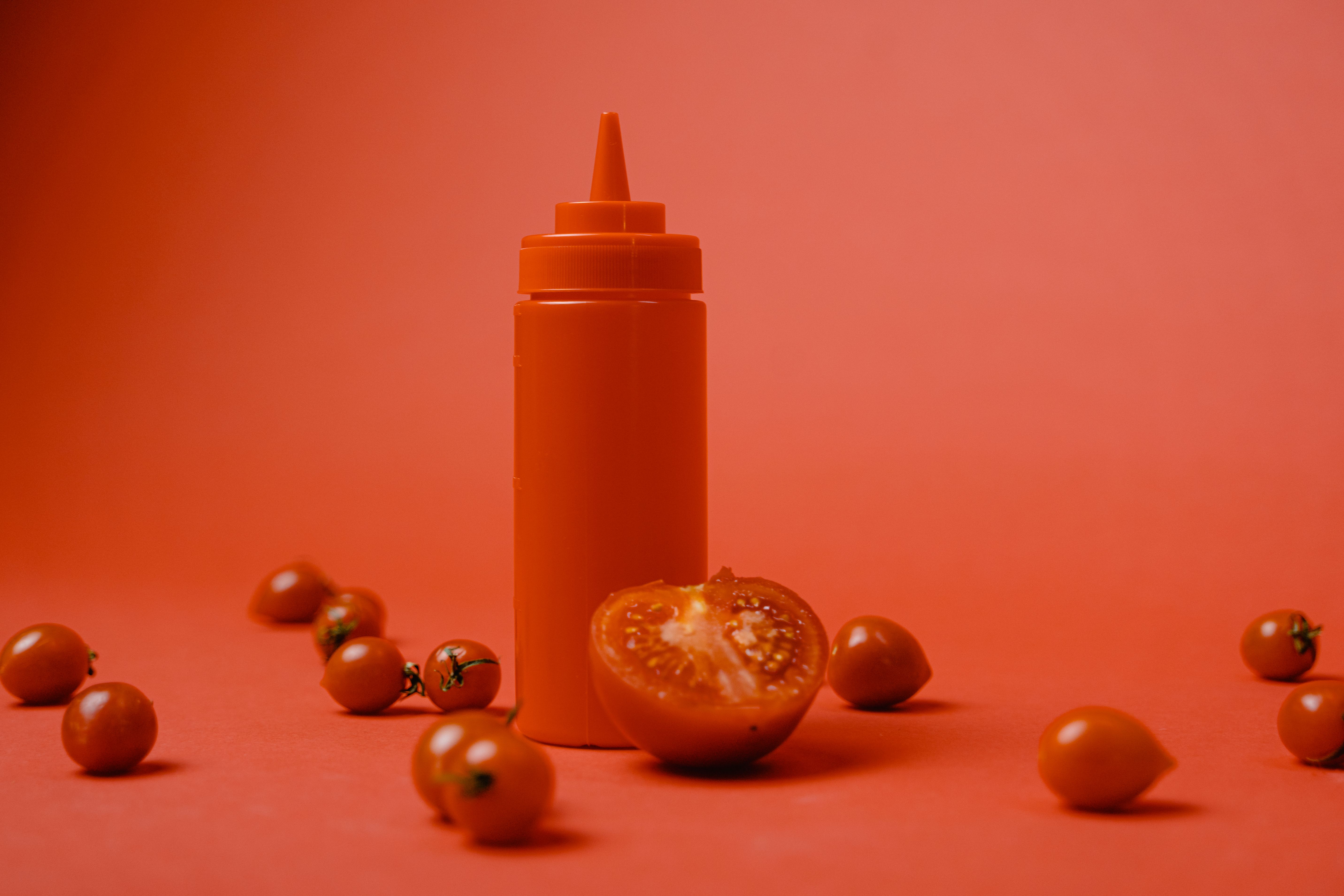 Artistic arrangement of cherry tomatoes and red squeeze bottle on a vibrant red background.