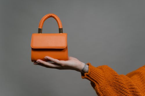 Free Stylish orange handbag held by a hand against a gray background. Perfect for modern fashion. Stock Photo