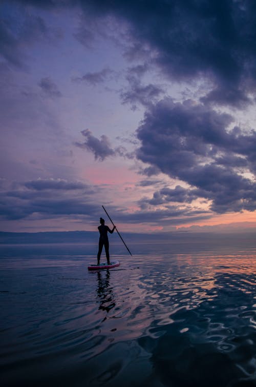 A Person Paddle Boarding at Sunset