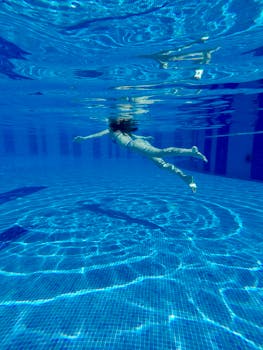 A lone swimmer gracefully underwater in a sunlit blue swimming pool.