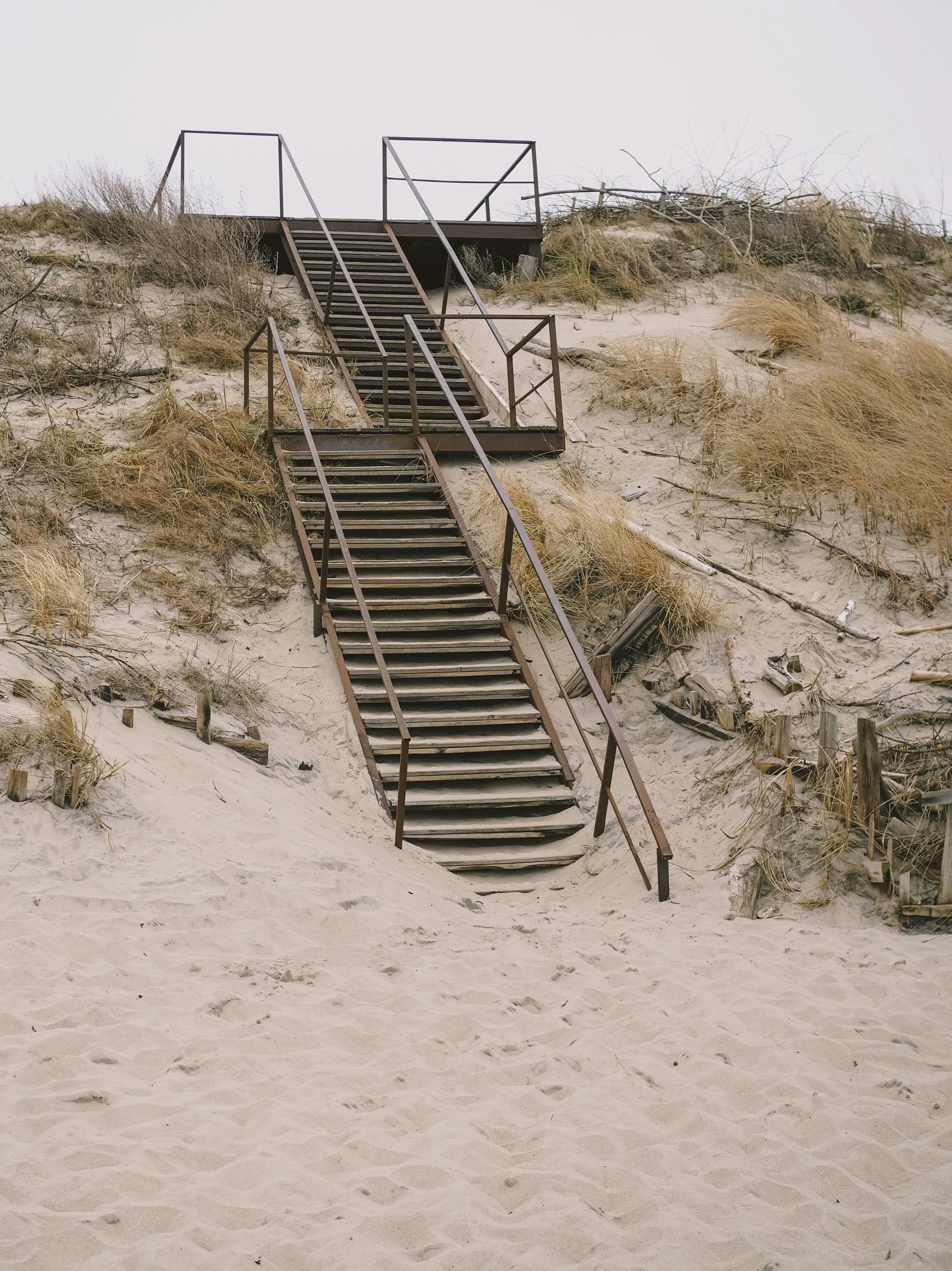 A metal staircase leads through sandy dunes, offering a rustic path to the top. Perfect for coastal adventure themes.