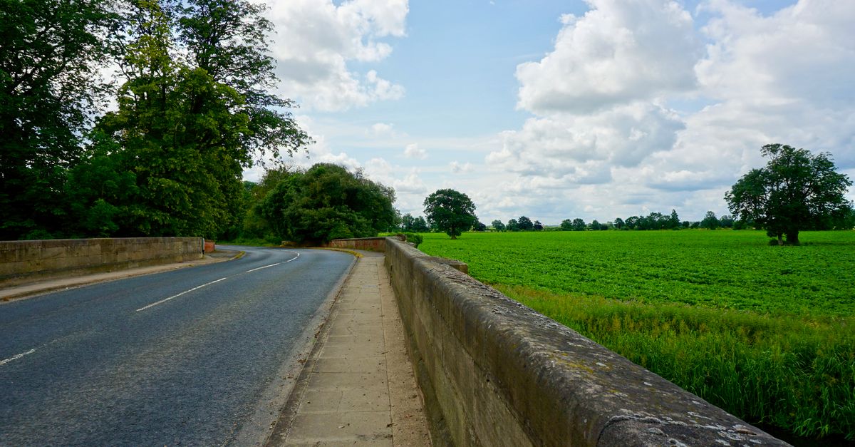 Beautiful summer landscape with a road through Market Deeping, England, surrounded by lush fields and clouds.